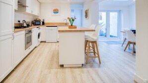 Una cocina moderna con armarios blancos, una isla central y una zona de comedor con sillas blancas.