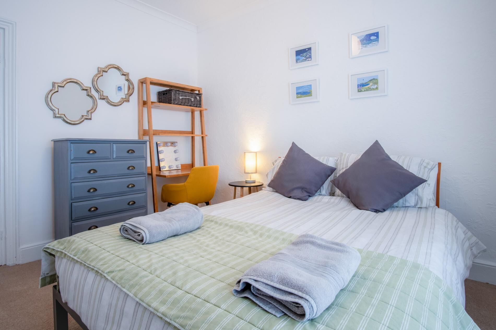 Una camera da letto ordinata con un letto, una cassettiera, una sedia, un comodino e decorazioni murali.