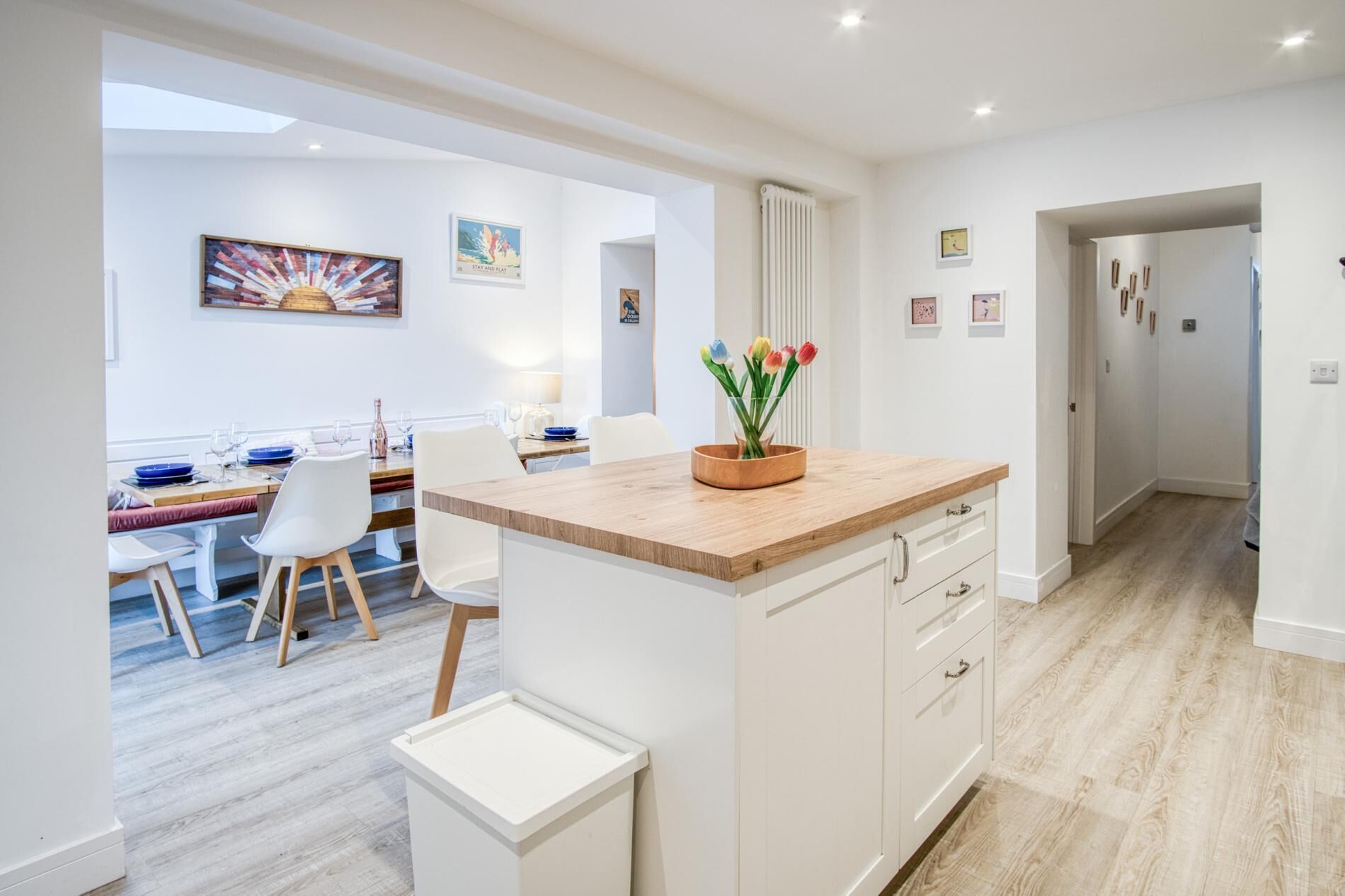 A modern kitchen with white cabinetry, a wooden countertop, and a small island with a vase of tulips.