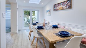 Un comedor con una mesa de madera dispuesta para cuatro, sillas blancas y una mesa con superficie de vidrio.