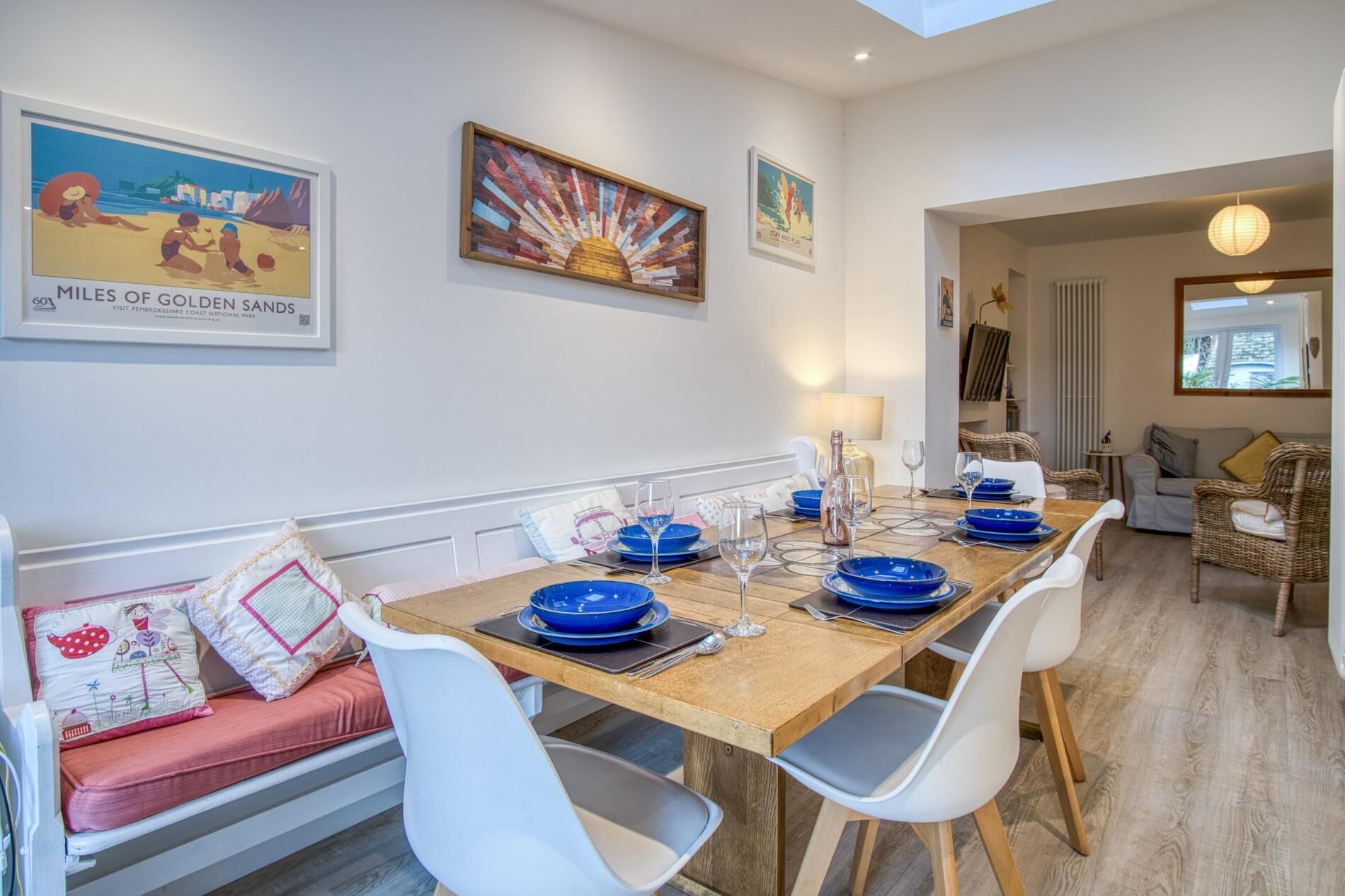 A dining area with a wooden table set for four, white chairs, and a bench with cushions.