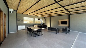 Eine moderne Küche mit einer großen Kochinsel, einem Essbereich mit Stühlen, einem eingebauten Fernseher und einer Decke mit Strohdeckung.