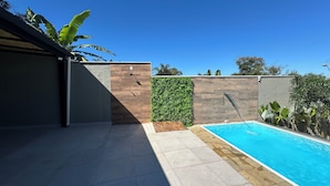 Ein moderner Poolbereich im Freien mit Holzterrasse, einer vertikalen grünen Wand und blauem Himmel.