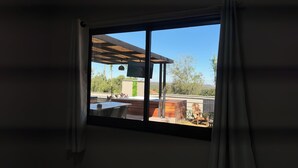 Ein Zimmer mit großem Fenster und Blick auf eine Terrasse mit Holzdeck, Gartenmöbeln und die umliegende Landschaft.
