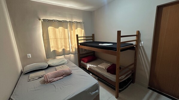 Une petite chambre avec un lit simple et un lit superposé, une fenêtre avec des rideaux et une porte.