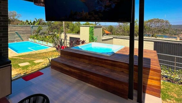 Eine moderne Terrassenanlage im Freien mit einem großen Flachbildfernseher, einem Holzdeck und einem Schwimmbecken.