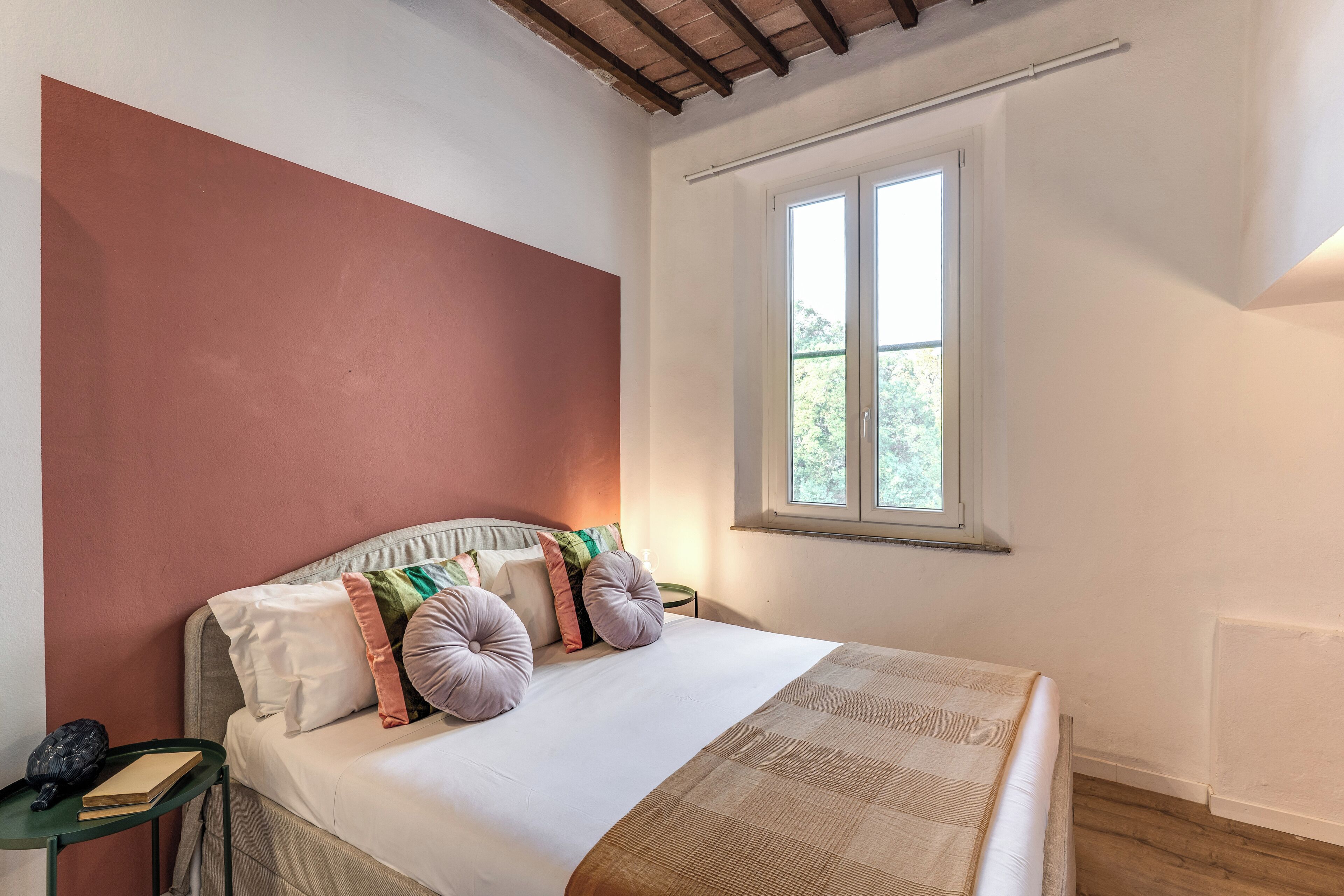 A bedroom with a bed, pillows, a bedside table, and a window.
