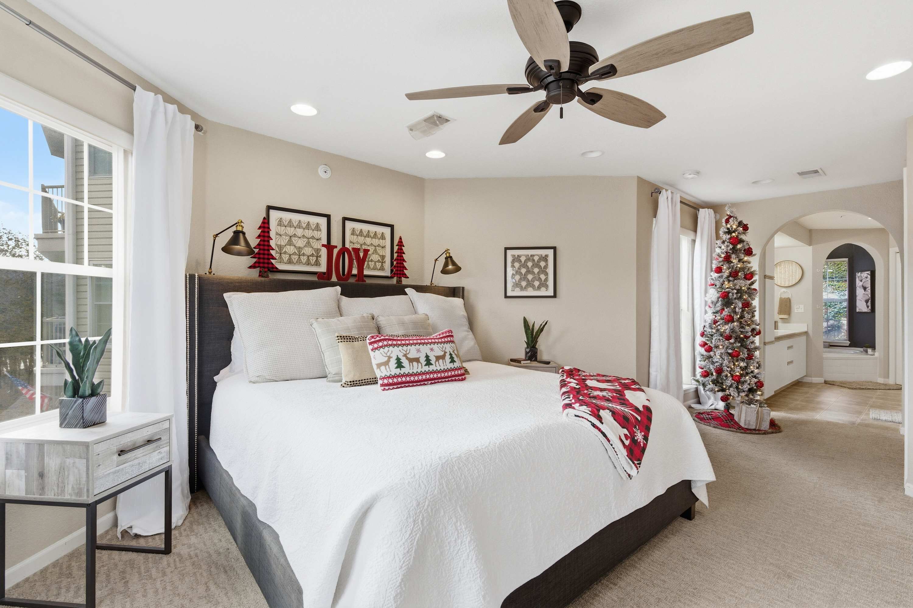 Ein Schlafzimmer mit einem Bett, einem Deckenventilator, einem Fenster und einem Weihnachtsbaum.