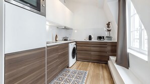 A modern kitchen with a built-in microwave, washing machine, and wooden cabinets. - ICONIC LANDMARKS THE LOUVRE MUSEUM ,TUILERIES GARDEN ARE JUST A STROLL AWAY (Paris)