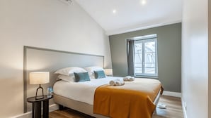 A modern hotel room with a large bed, a nightstand, a lamp, and a window with a view of buildings. - ICONIC LANDMARKS THE LOUVRE MUSEUM ,TUILERIES GARDEN ARE JUST A STROLL AWAY (Paris)