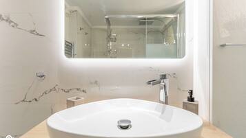 Un baño moderno con un lavamanos ovalado grande, un espejo y una ducha.