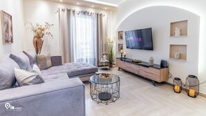Una sala de estar moderna con un sofá gris, una mesa de centro de vidrio, un televisor montado en la pared y una decoración de estilo minimalista.