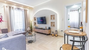 Una sala moderna con un sofá, una mesa de comedor para dos personas, un televisor montado en la pared y una decoración minimalista.