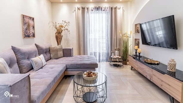 Una sala de estar moderna con un sofá seccional, una mesa de centro de vidrio, un televisor de pantalla plana y un jarrón decorativo.