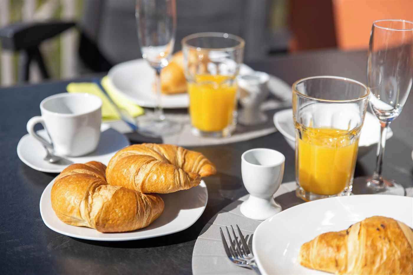 A breakfast setting with croissants, orange juice, and coffee cups on a table.