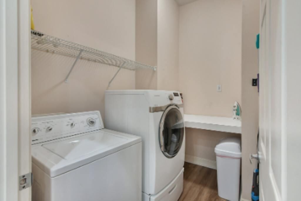 A laundry room with a washer and dryer, a small trash can, and a shelf with a bottle.