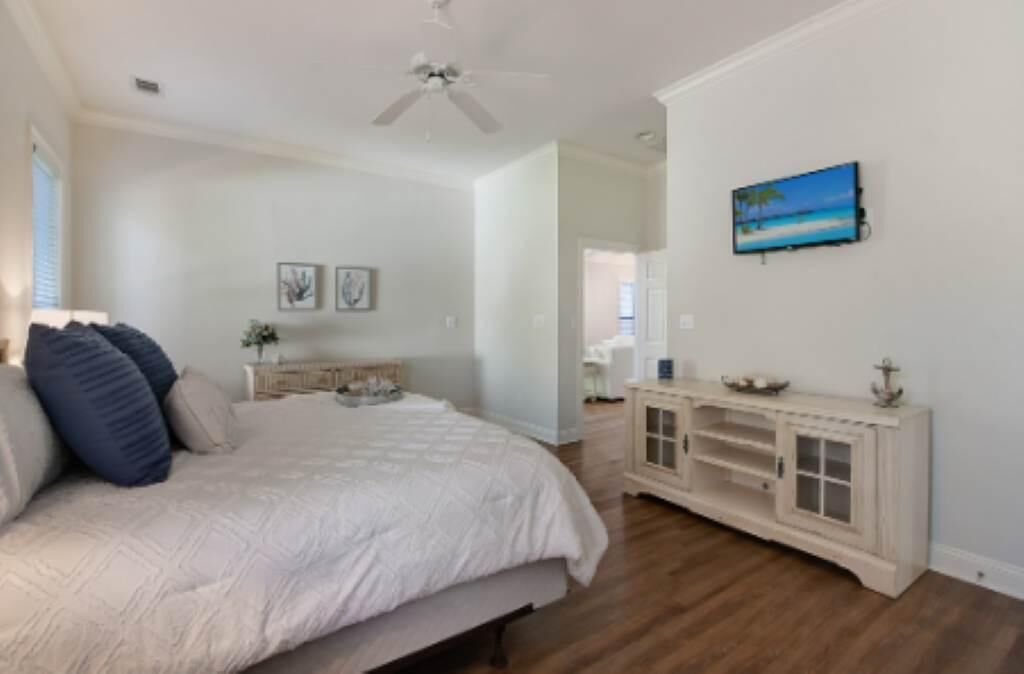 A bedroom with a bed, a ceiling fan, a TV on the wall, and a console table.