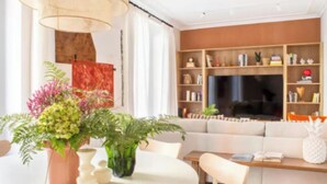 A modern living room with a sofa, a coffee table, and a TV. There are decorative plants and a bookshelf with various items. - Bright & Spacious 3-Bedroom Apartment in the Heart of Madrid (Madrid)