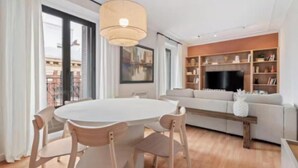 A modern living room with a round dining table, light-colored chairs, a sofa, a TV, and a bookshelf. - Bright & Spacious 3-Bedroom Apartment in the Heart of Madrid (Madrid)