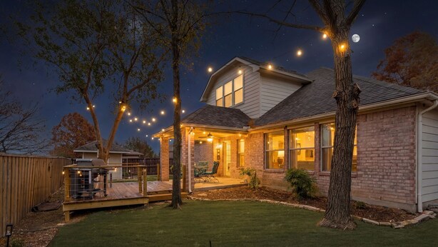 Una casa residencial con césped cuidado, una terraza y luces colgantes.