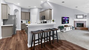 Una cocina moderna con una isla central, taburetes de bar y una chimenea en la sala de estar.