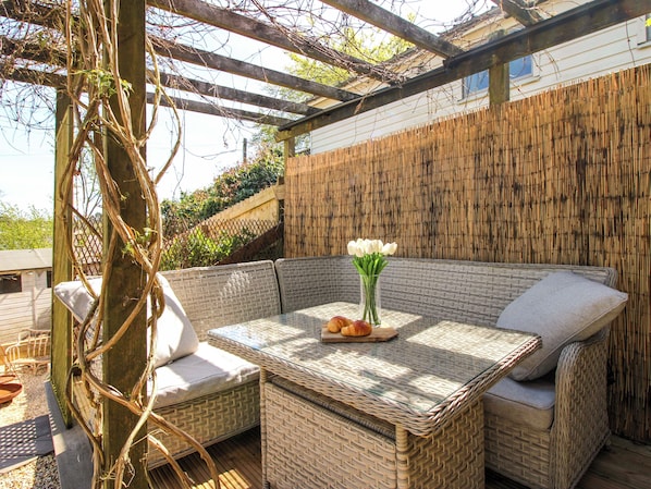 Un espacio de estar exterior de mimbre con mesa, cojines y un jarrón de flores.