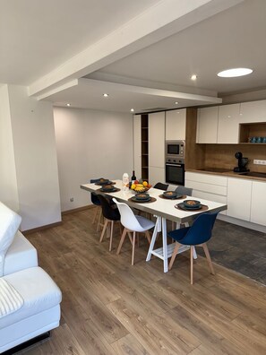 A modern dining area with a white table, blue chairs, and a kitchen with white cabinets and a wooden countertop. - Villa 400 m from the beach (Labenne)