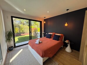A modern bedroom with a large bed, a potted plant, and a view of a garden through a sliding door. - Villa 400 m from the beach (Labenne)