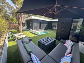 Ein moderner Außenbereich mit Pool, überdachter Sitzgelegenheit und einem zeitgemäßen Haus im Hintergrund.