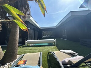 Ein moderner Außenbereich mit zwei Liegestühlen, einem Pool und einer Palme.