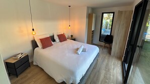 Quarto moderno com uma cama grande, mesas de cabeceira, um criado-mudo, uma cadeira e uma janela ampla.