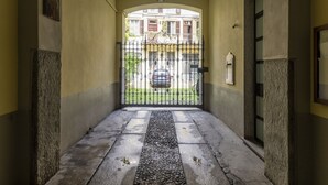 Ein Gang mit Steinboden, einem Metallgitter und Blick auf einen geparkten Wagen vor dem Haus.