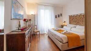Ein Hotelzimmer mit einem Bett, einer Holzkommode, einem Schreibtisch, einem Sessel, einer Karte an der Wand und einem Fenster mit Vorhängen.