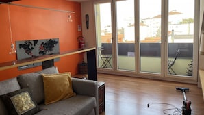 Ein Wohnzimmer mit grauem Sofa, einer Weltkarte an der Wand und einer großen Schiebeglastür, die zu einem Außenbereich führt.