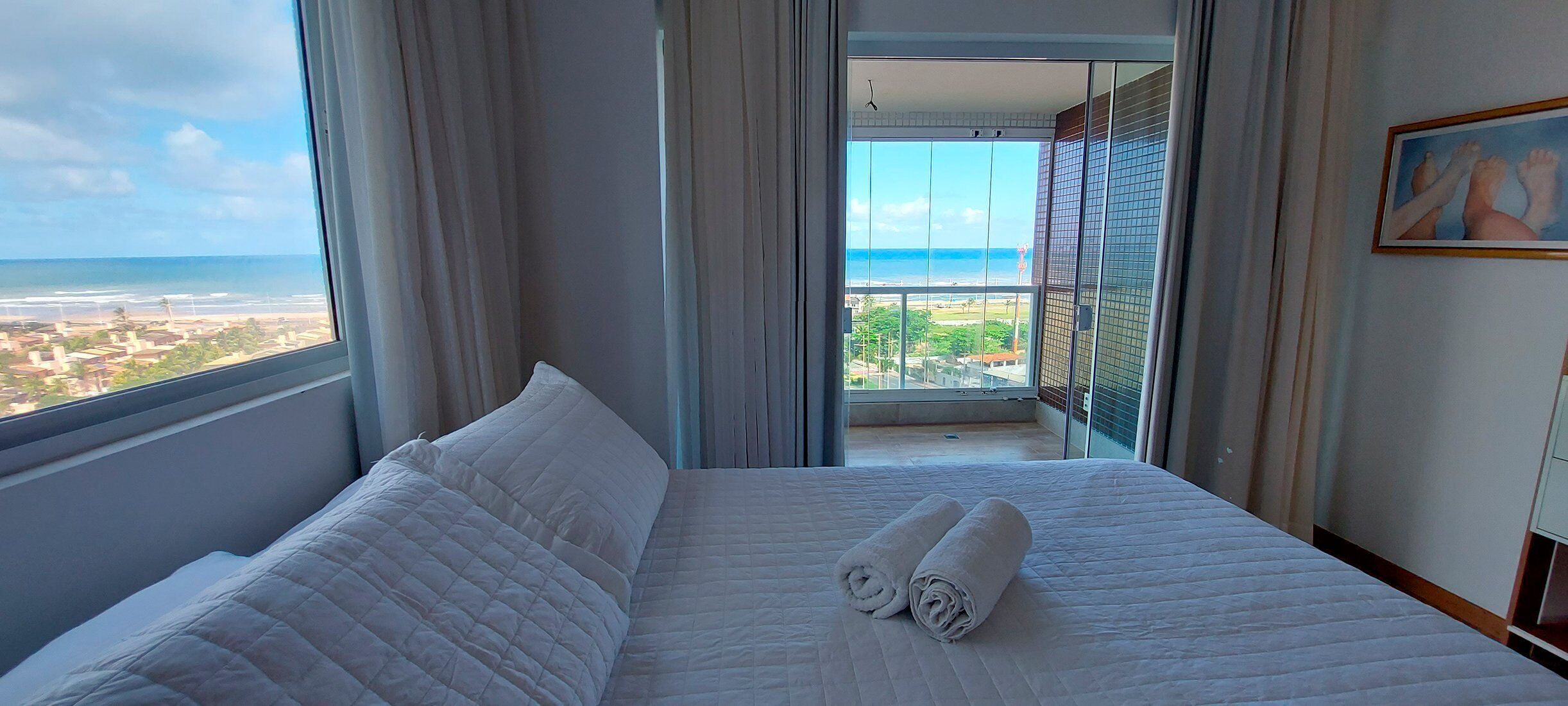 Quarto de hotel com uma cama grande, vista para a praia e uma varanda com guarda-corpo.
