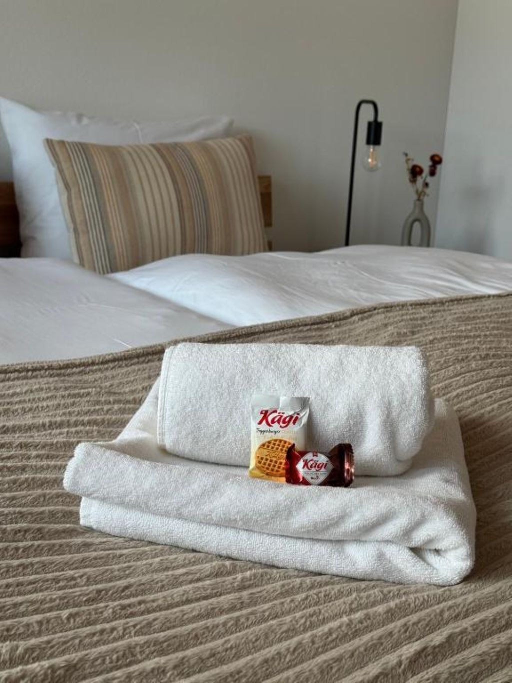 Un lit bien fait, avec un oreiller à rayures, une couverture blanche et une serviette pliée posée sur le dessus.
