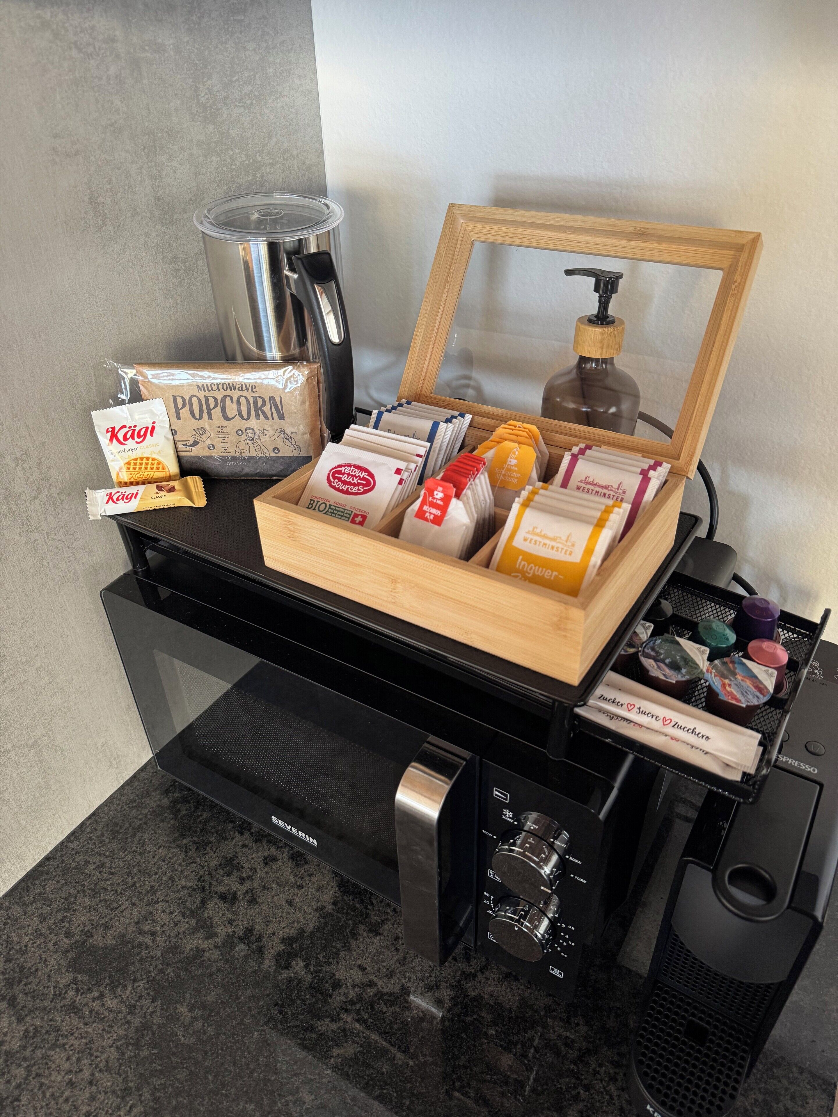 Een kitchenette met een magnetron, waterkoker en koffieapparaat. Op het aanrecht staan snacks en kruiden.