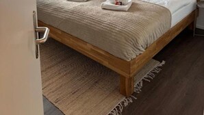 A bedroom with a wooden bed, a window with curtains, a bedside table, and a wall-mounted artwork.