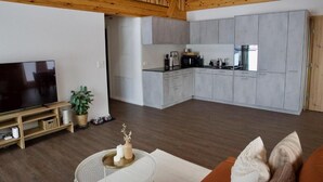 A modern living room with a flat-screen TV, a sofa, and a kitchen area with grey cabinets and a black countertop.