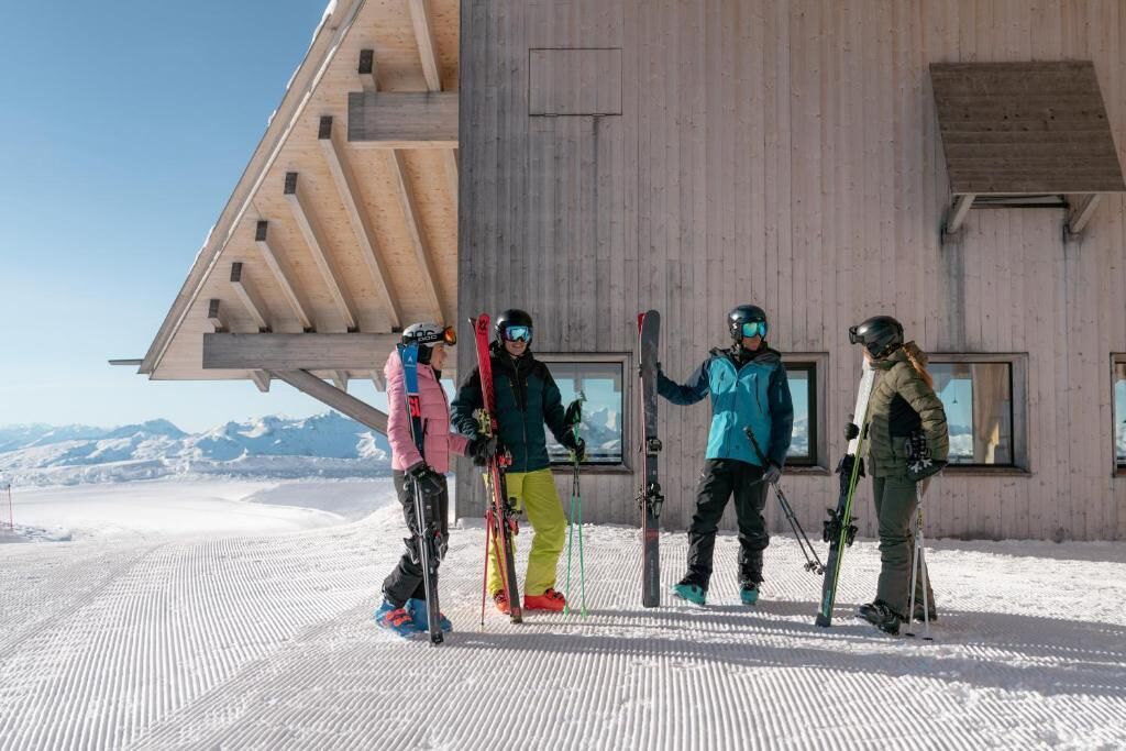 Un grupo de esquiadores en una pendiente nevada, con un edificio de madera al fondo.