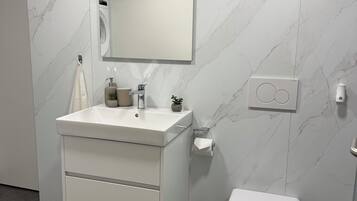 Een moderne badkamer met een wit badkamermeubel, een spiegel, een toilet en een prullenbak.