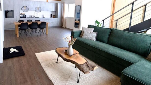 A modern living room with a green sofa, wooden coffee table, and a dining area with a wooden table and chairs.