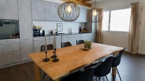 A spacious dining area with a wooden table and chairs, a kitchen in the background, and a high ceiling with exposed beams.