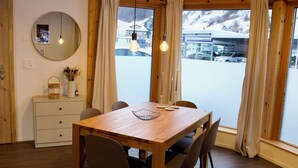 A wooden dining table with chairs, a mirror, and a vase with flowers on a dresser.