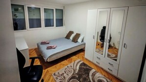 Une chambre à coucher comprenant un lit, un bureau, une chaise, une armoire et une fenêtre avec des stores.