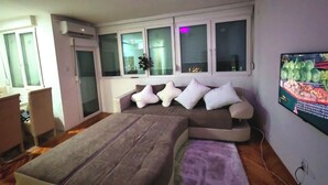 Un salon moderne avec un canapé d’angle, une petite table et un téléviseur à écran plat fixé au mur.