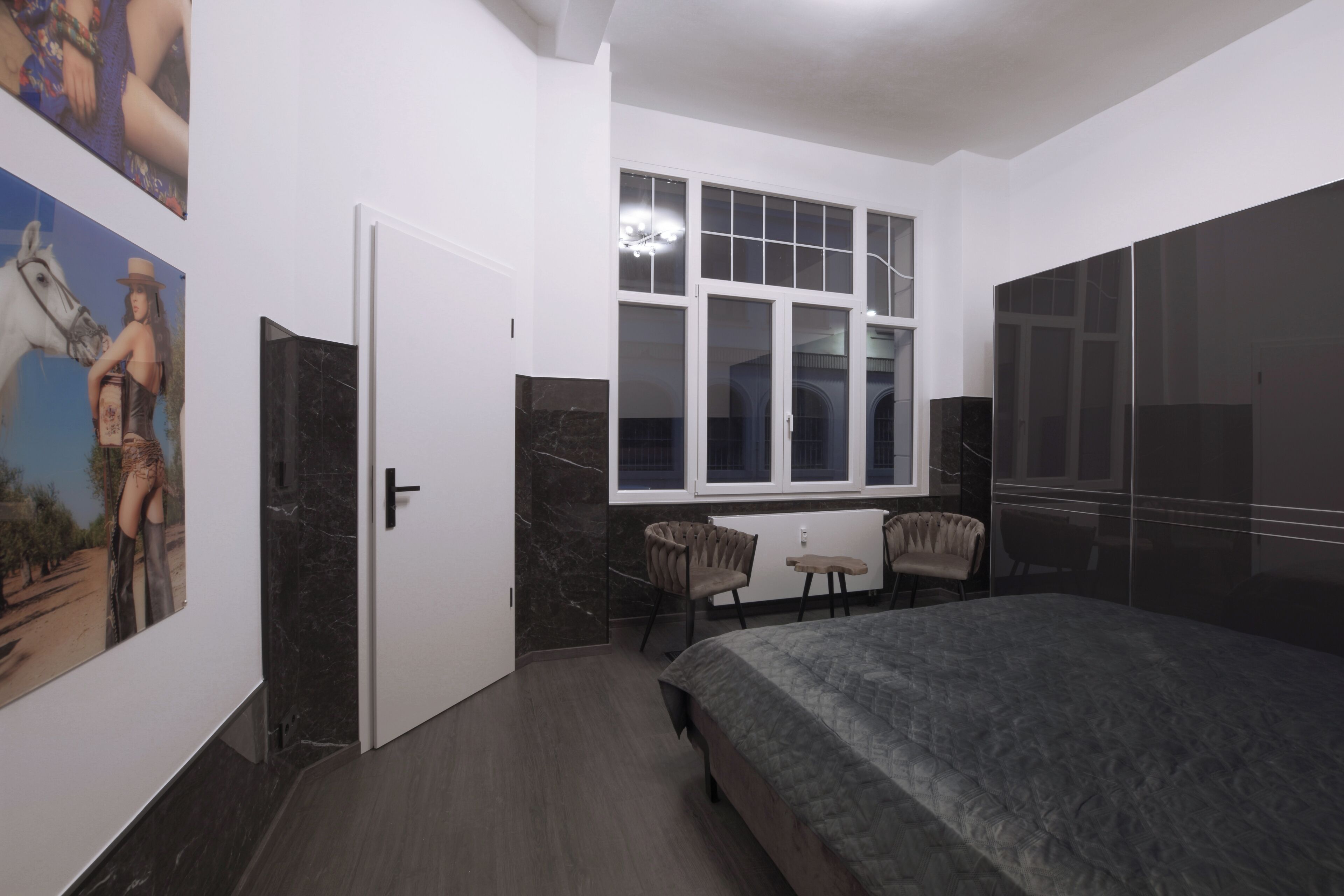 A bedroom with a bed, a desk, two chairs, a window, and a door.