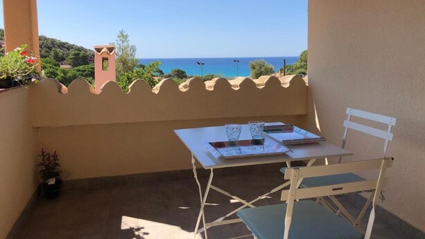 Un balcon avec une table et des chaises, offrant une vue panoramique sur la mer et les collines.