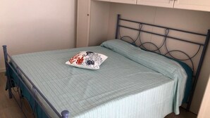 Un lit simple avec un cadre en métal et une couvre-lit bleu clair, un coussin décoratif et des placards blancs au-dessus.