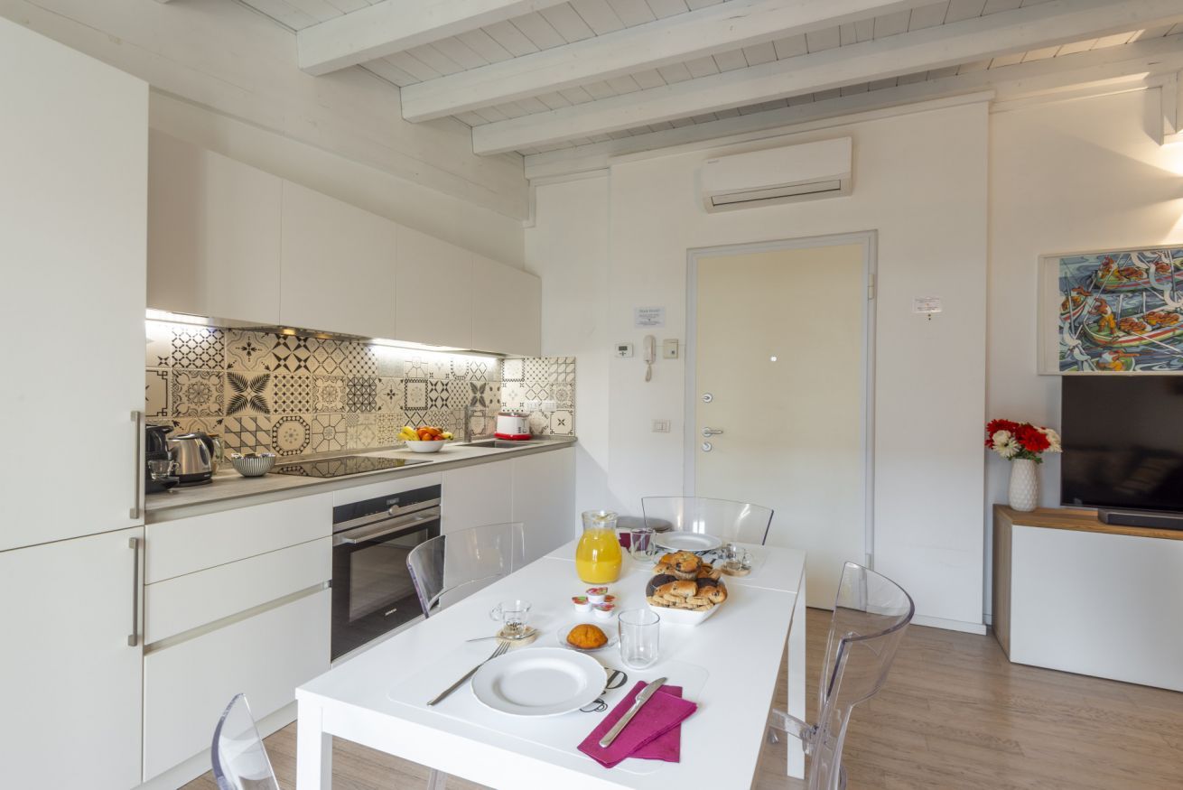 A modern kitchen with white cabinetry, a dining area with a table set for breakfast, and a TV in the living area.